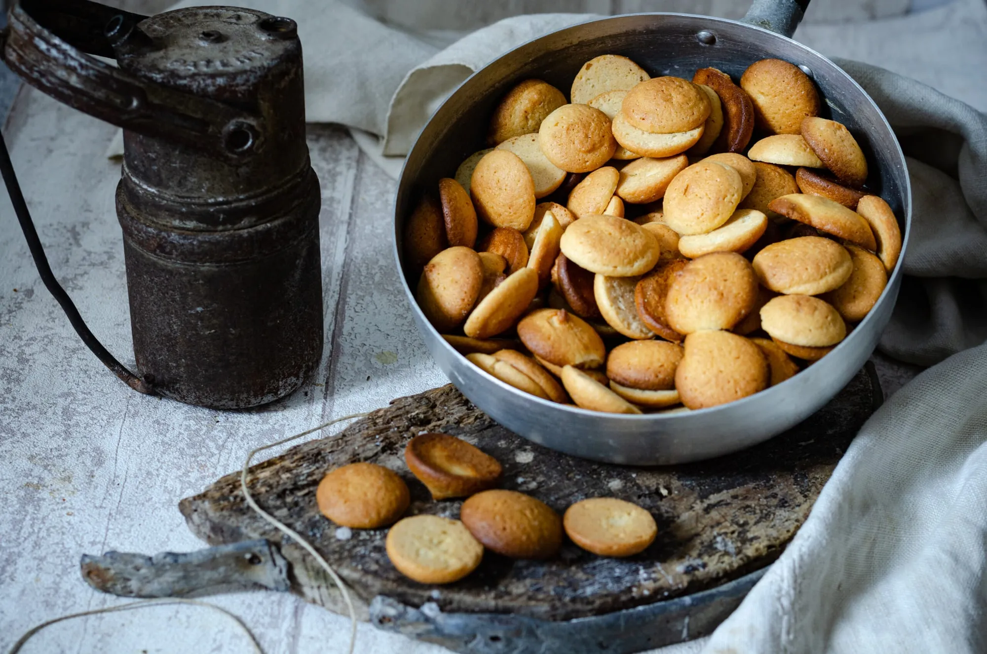 Galletas de nata finas y doradas en una lata, junto a un molinillo antiguo